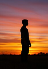 A serene silhouette of a person, standing against a vibrant sunset background in the open field.