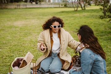 A young, brown-skinned woman enthusiastically tells her young, Asian female friend something as...