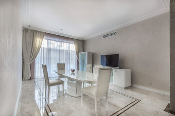 Fototapeta premium Elegant dining room of a country house with white furniture and a TV. The room with a panoramic window is decorated in pastel colors.