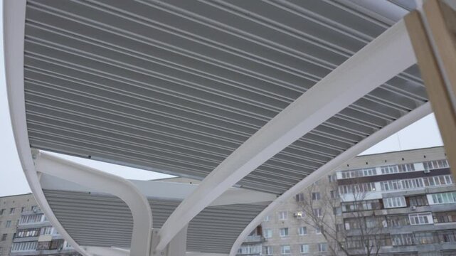 Stylish metal canopy above benches offers shelter from snow and sun. Structure creates cozy all-weather resting place for visitors