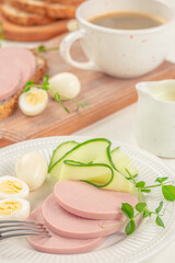 Healthy breakfast with sliced sausage, quail eggs, cucumber ribbons, and black coffee.