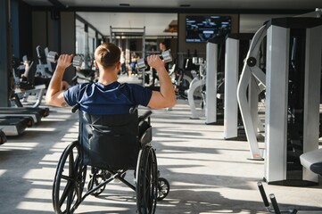 Man in wheelchair lifting dumbbells during rehabilitation in gym