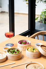 Wild mushroom dim sum, Cantonese prawn dumpling, and crystal vegetable dumpling served with dipping sauces and chopsticks, paired with a red cocktail on a restaurant table.