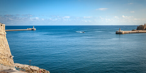 A boat enters the sea gate . Seascape with lighthouses and the walls of the city of Valletta, Malta.