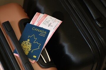 Canadian passport with tickets lies on touristic suitcase close up in airport waiting hall. Travel worldwide and international tourism concept