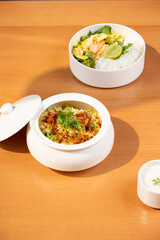 Aromatic veg biryani with saffron, herbs, and paneer served in a lidded white pot beside turmeric lemongrass seafood rice—paired with curd, sunlit on a brown table in a cozy restaurant.   