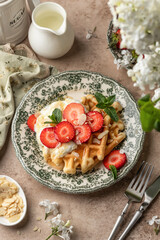 Homemade belgian waffles with strawberries, whipped cream and honey. Served on a rustic plate with spring flowers