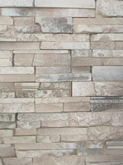 Beige artificial stone wall close-up with rectangular textured blocks, architectural surface background for exterior or interior design
