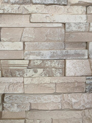 Beige artificial stone wall close-up with rectangular textured blocks, architectural surface background for exterior or interior design