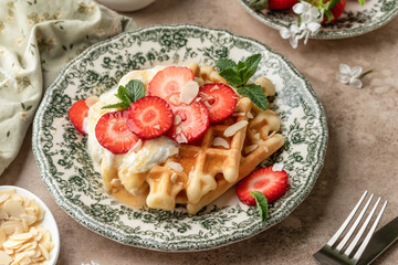 Homemade belgian waffles with strawberries, whipped cream and honey. Served on a rustic plate with spring flowers