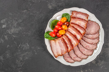 Top view of assorted sliced ham and fresh cherry tomatoes on a white plate over dark background