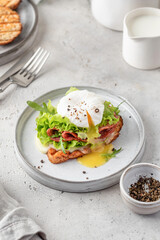 Toasted bread with poached egg, salad, cheese and ham on a plate on white kitchen background. Healthy breakfast, diet food