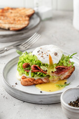 Toasted bread with poached egg, salad, cheese and ham on a plate on white kitchen background. Healthy breakfast, diet food