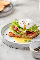 Toasted bread with poached egg, salad, cheese and ham on a plate on white kitchen background. Healthy breakfast, diet food
