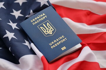 Ukrainian biometrical passport on folded waving flag of United States of America