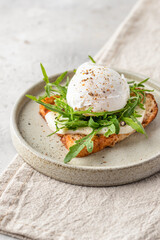 Toasted bread with poached egg, cheese and arugula on a plate on white kitchen background. Healthy breakfast, diet food