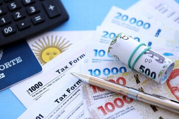 Argentine pesos money bills in big amount lies on table with pen, calculator, passport and tax forms