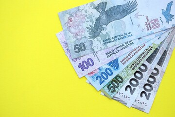 Argentine pesos money bills in big amount lies on yellow color table close up
