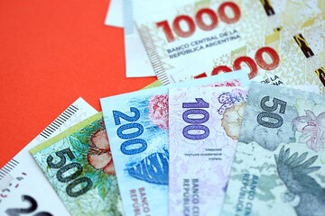 Argentine pesos money bills in big amount lies on red color table close up