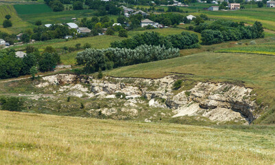 Obraz premium Rural landscape with eroded limestone cliffs and distant village houses in summer