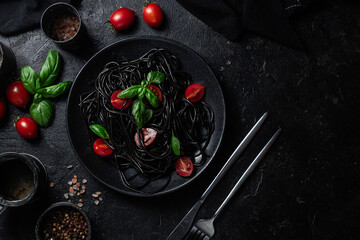 Black Spaghetti with  Cherry Tomatoes, and Basil in a black plate on a dark background.