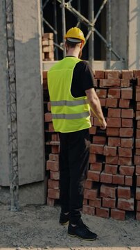 Ouvrier barbu sur chantier posant avec un pouce lev&eacute; devant des briques

