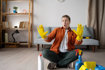 Housekeeping job. Young woman in casual clothes sitting on floor with cleaning supplies, washing...