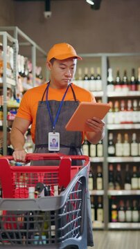 Asian serious sellerman employee worker standing at alcohol section using tablet computer for work. Grocery store. Supermarket.