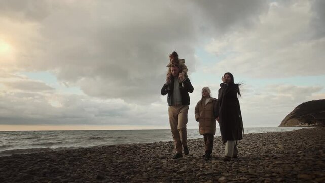 father mother and daughters stroll along beach