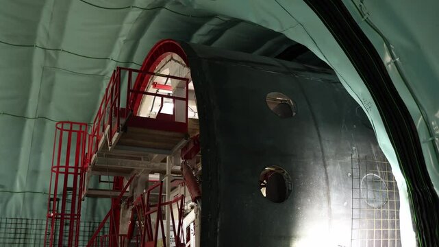 Tunnel formwork structure with bright red safety railings and sealed green insulation creates a striking contrast industrial lighting and smooth metal panels emphasize precision and active progress