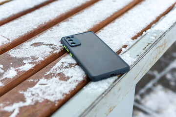 A mobile phone accidentally left on a snowy bus stop bench.