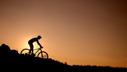 Fototapeta premium Silhouette of Mountain Biker: Capturing a mountain biker's silhouette conquering a rugged slope at sunrise. Emphasizing the adventure, silhouette, sport, and challenge of the great outdoors.