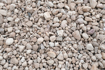Textured surface of small gravel stones in various shades of gray and beige, creating a natural background for landscaping, construction, or decorative purposes. Copy space