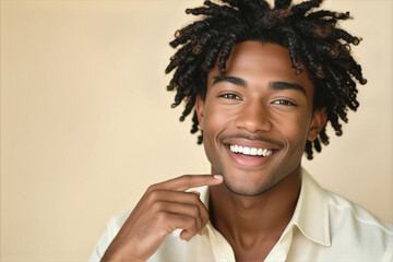 A young Black man with dreadlocks smiles warmly at the camera, gently touching his chin in a portrait-style photograph.