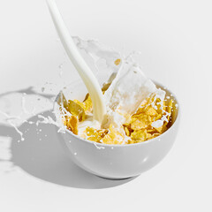 Milk pours and splashing violently into white bowl full of cornflakes, frozen in dynamic motion with drops flying outward. Concept of nutrition, catering, traditional, fast food, takeaway