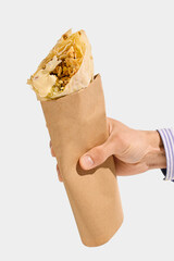 Shawarma roll with grilled meat, white sauce, cabbage, and flatbread held in brown paper sleeve, viewed from hand against white background. Concept of shawarma, wrap, meat, takeaway, street food