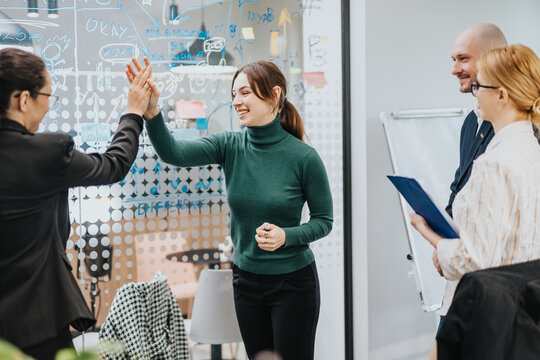 A group of focused employees in a professional office interacting during a creative brainstorming session. Celebrating success through teamwork and high-fives in a productive work atmosphere.