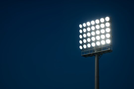 Bright stadium floodlights against a dark blue night sky, copyspace; concept for sports events, advertising, and broadcasting