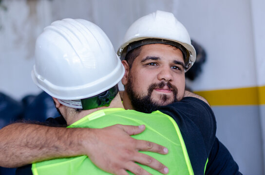Factory workers hugging.Friendly industry workers at construction site wearing safety hats - Powered by Adobe