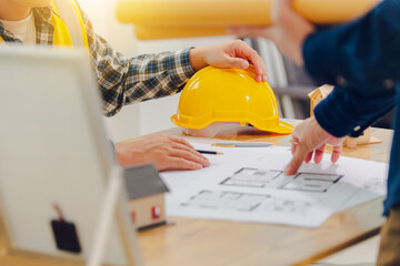 Architects and solar engineers discuss home design in office using model homes, solar panels, and architects' design documents. Concepts about home construction and solar power.