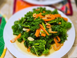 Stir-fried kale, chopped garlic and carrots with dried shrimp. Healthy food, organic kale stir-fried with oyster sauce served on white round plate, Brassicaceae vegetable, not bitter full of nutrients