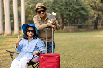 Indian senior traveler couple holding a red suitcase and passport with a flight ticket at outdoor