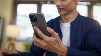 Smiling young businessman reading something on his smartphone while working at his desk.