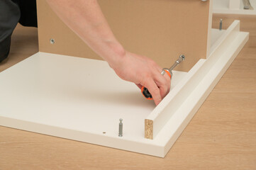 An individual is constructing furniture using a screwdriver