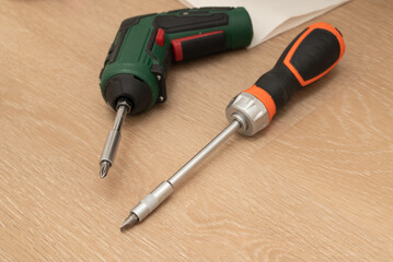 A common screwdriver and a power drill are both resting on a wooden surface