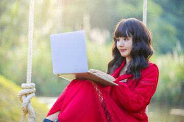 Beautiful confident asian businesswoman working with laptop, Hands typing keyboard. Online chat. Spend free time on the swing. Sunrise beam in the beautiful park.