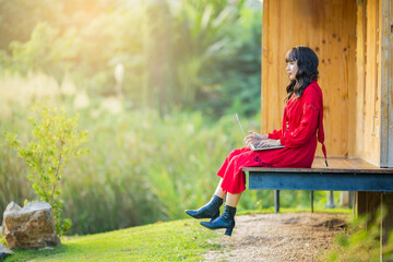 Attractive asian woman working on a laptop on the terrace overlooking the green jungle on a bright sunny day.