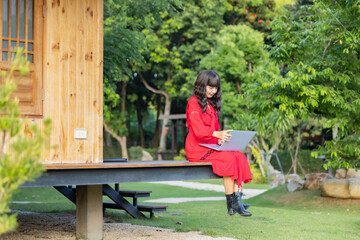 Focused asian woman watching webinar on laptop, writing blog or email, remotely online work in her home garden surrounded by plants. Nature view of green leaf in garden under sunlight in the afternoon