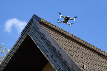 Drone in the air inspecting the roof over the house closeup blue sky