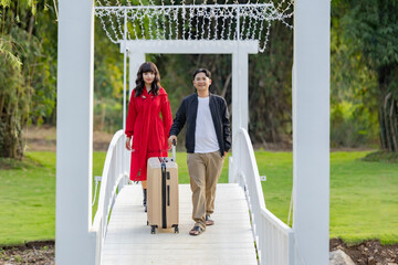 Beautiful young happy couple of tourists walking with luggage at countryside homestay surrounded by green forest Concept of people and healthy natural lifestyle.